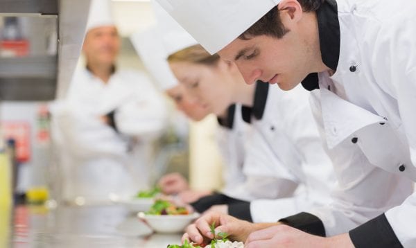Culinary Class In Kitchen Making Salads As Teacher Is Overlooking